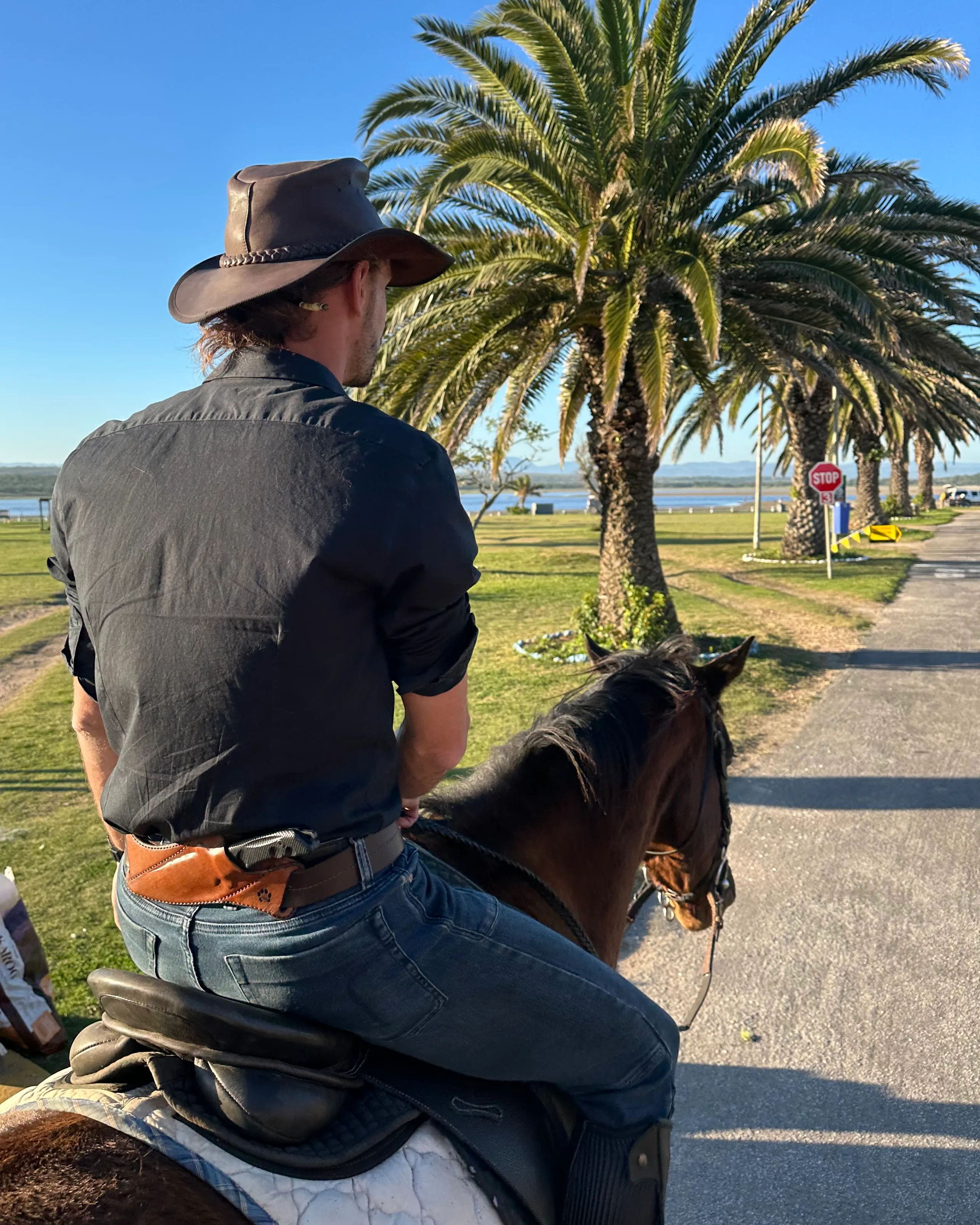 Theuns, in a brown hat, riding away from the camera past palm trees